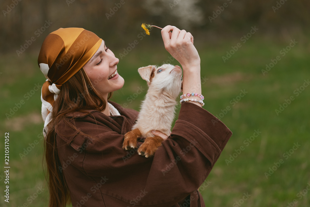 Obraz premium Smiling woman in a brown cloak embraces a playful goat kid outdoors, a warm lifestyle moment with nature, affection, and gentle light creating a cozy, intimate mood.