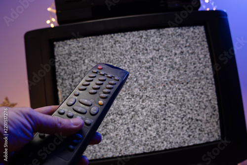 Hand holding television remote control in front of static noise screen