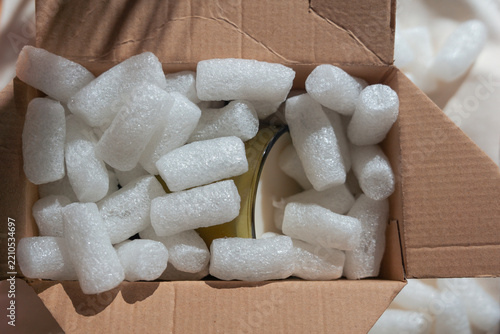 biodegradable starch packing peanuts white loose fill packaging material in cardboard box, eco friendly water soluble cushioning protecting glass jar during shipping, top view close up