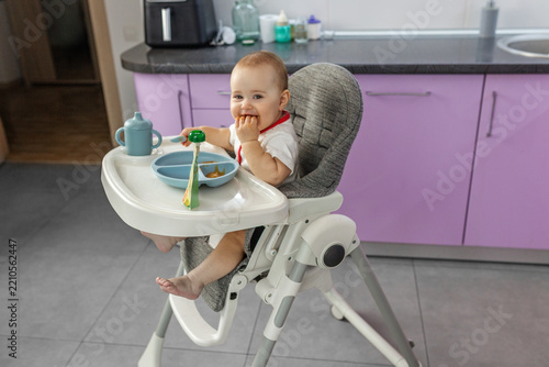 Happy baby eating finger food in high chair side view