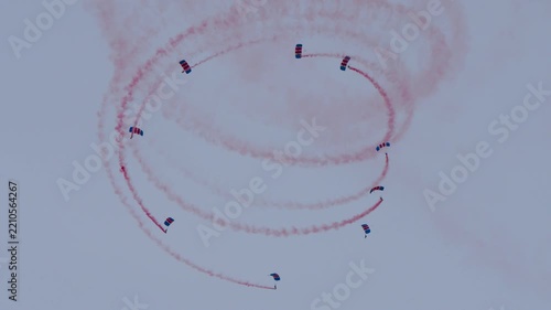 Parachute team falling in a circle formation with red smoke trails