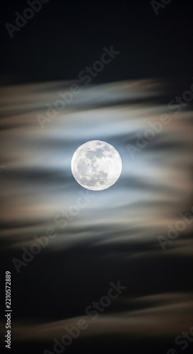 Thin clouds moving rapidly across the face of a bright full moon at night