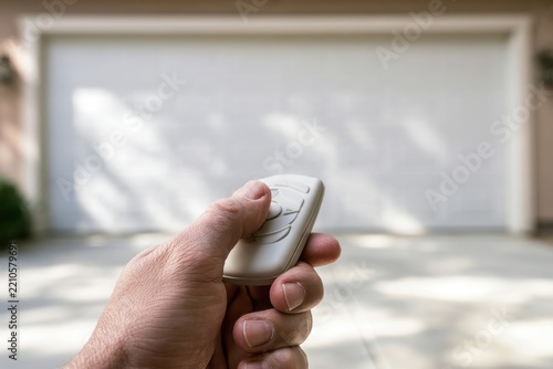 Manual operation of a garage door: close-up hand with remote in front of a suburban garage