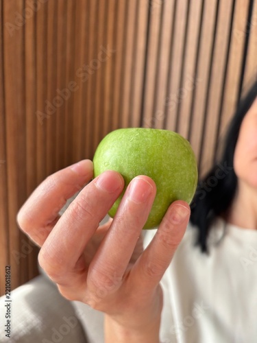 Woman holding fresh green apple toward camera, healthy eating and nutrition concept