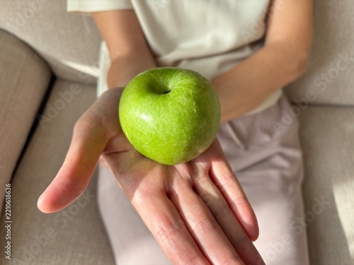 Woman presenting fresh green apple on open palm, healthy nutrition and food choice concept