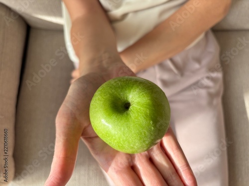 Woman presenting fresh green apple on open palm, healthy nutrition and food choice concept