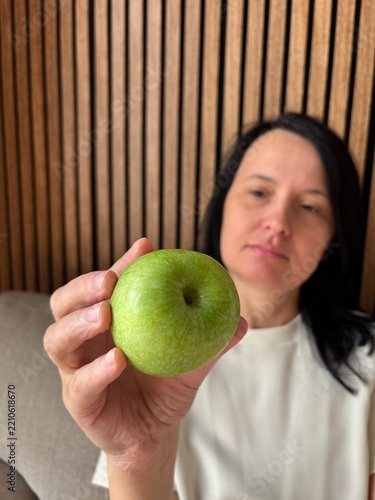 Woman holding fresh green apple toward camera, healthy eating and nutrition concept