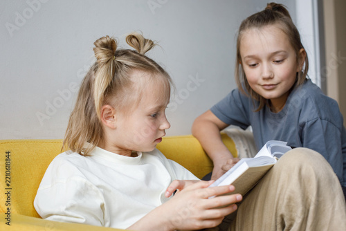 Smiling children reading a book at home. Blonde sibling 11 and 7 years old