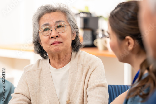 Senior Asian woman discusses health concerns with female nurse in assisted living center, receiving compassionate listening, emotional support, wellness guidance and reassuring nursing care.