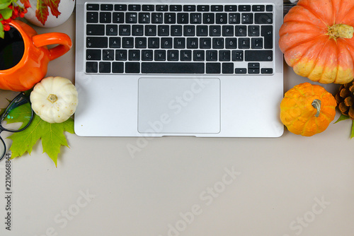 workspace with laptop, pumpkins, coffee cup, glasses and colorful fall leaves on a neutral desk with copy space.