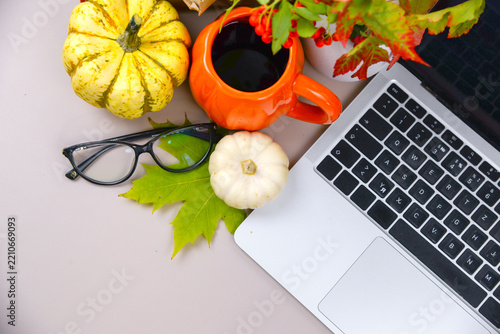 workspace with laptop, pumpkins, coffee cup, glasses and colorful fall leaves on a neutral desk with copy space.