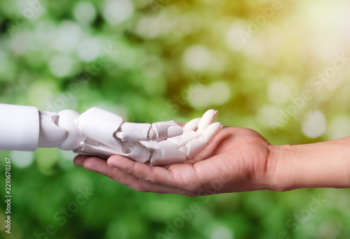 Human Hand Holding Robotic Hand on Green Nature Background for Eco AI Concept