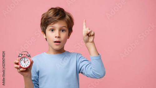 Surprised boy holding alarm clock and pointing up