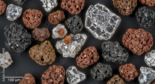 Microscopic view of diverse mineral particles and crystalline structures on a dark background