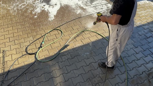 Professional worker pressure washing paved driveway surface
