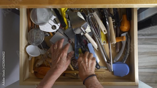 A woman looking for a kitchen utensil in a cluttered drawer