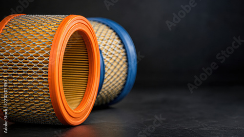 Two cylindrical air filters with orange and blue rims rest on a dark surface against a black background.