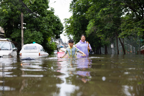 Asian boy wearing Raincoat and mother waded through floodwaters to go buy food, lifestyle of Thai people in massive flooding, Severe weather