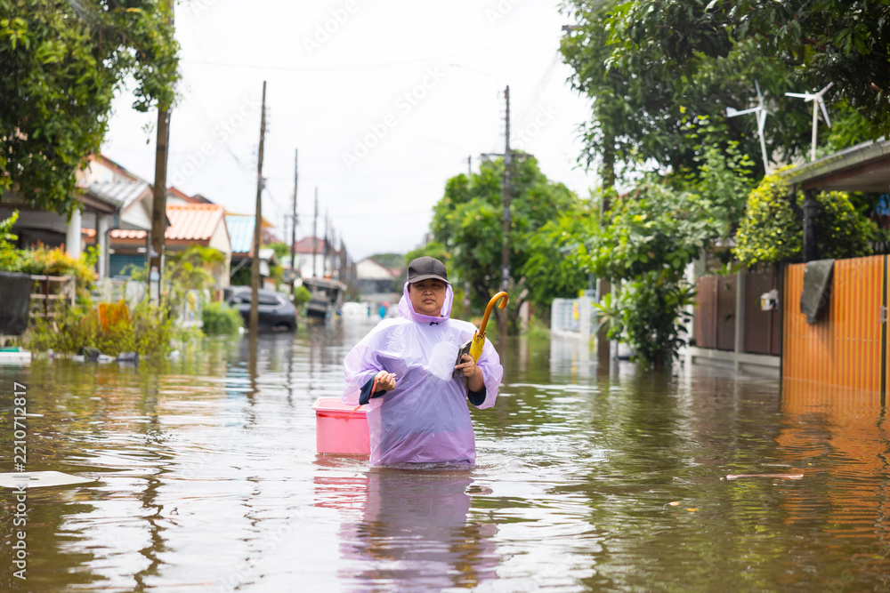 Fototapeta premium obese woman wearing Raincoat and walking through flood waters to go buy food, lifestyle of Thai people in massive flooding, Severe weather