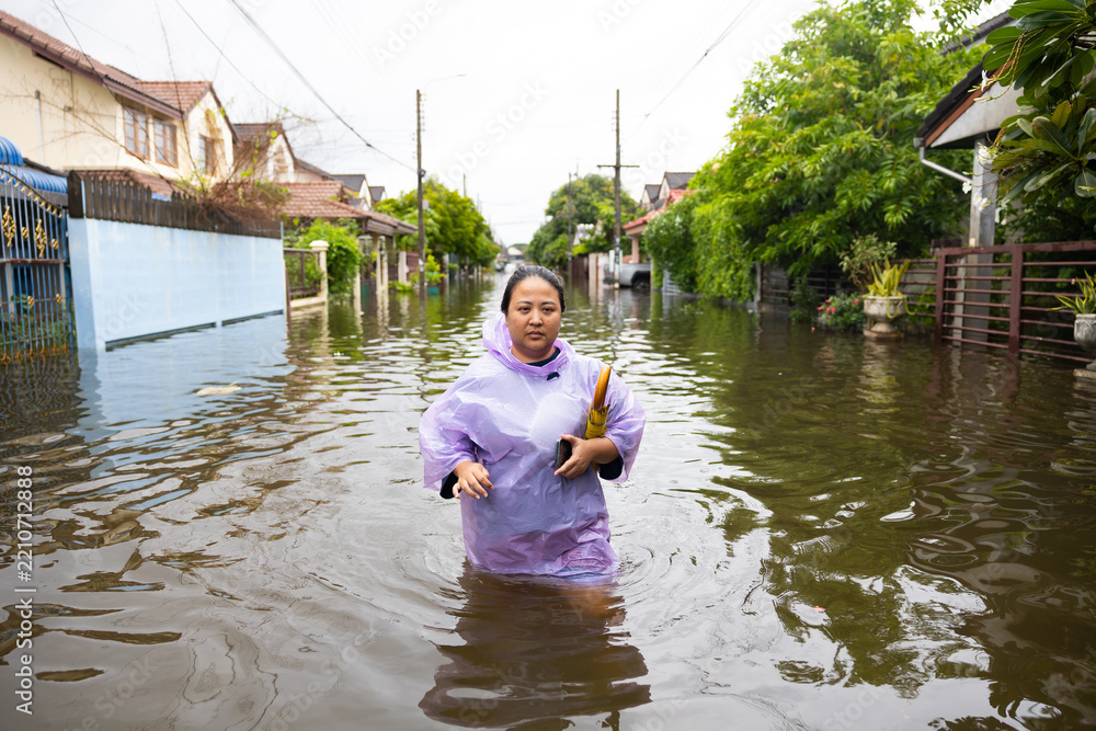 Fototapeta premium obese woman wearing Raincoat and walking through flood waters to go buy food, lifestyle of Thai people in massive flooding, Severe weather