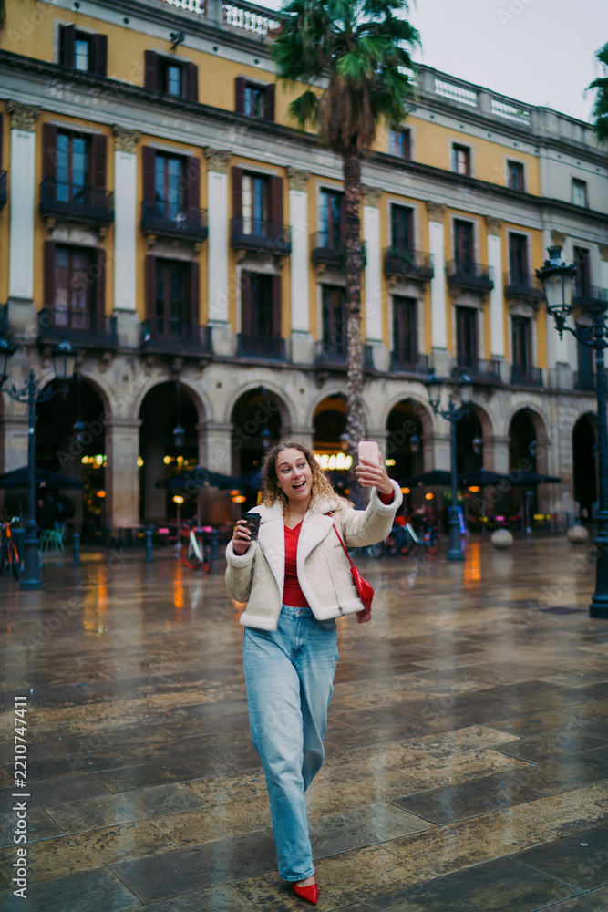 Obraz premium Excited woman taking selfie on city square, making video call, blogging influencer, 5G wireless technology, mobile app, authentic representation, digital nomad, urban travel lifestyle.