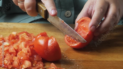 Slicing fresh red tomatoes with a knife on a cutting board on a wooden table