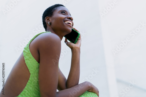 African American woman mobile call talking. Black female model using cellphone network roaming during trip, laughing while discussing international travel route near white wall copy space.