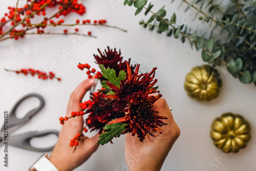 Hands arranging autumn bouquet with chrysanthemums and red berries