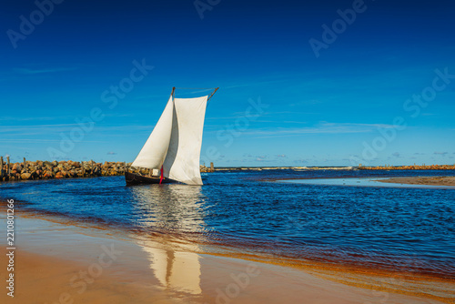 A sailboat with white sails in the beach of the Baltic sea
