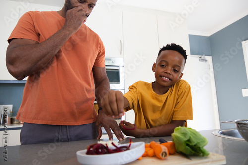 African American father and son preparing vegetables in home kitchen with board, carrots