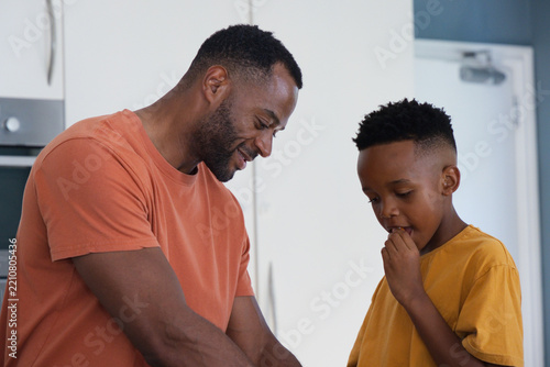 African American father in rust shirt and son in mustard shirt tasting batter at kitchen counter