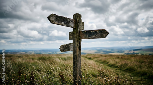 An old weathered wooden signpost standing in the middle of a grassy field under a dramatic cloudy sky landscape