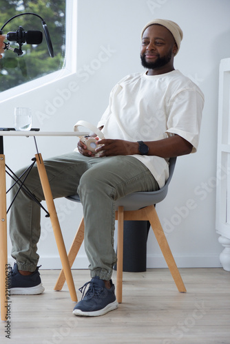 African American man wearing beanie holding white headphones speaking into boom mic in studio