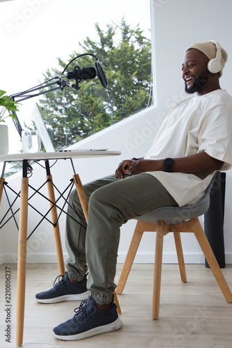 Man wearing beanie and headset recording podcast sitting at home studio with boom mic, copy space