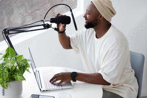 African American man in beanie recording with boom mic operating laptop at home studio, copy space