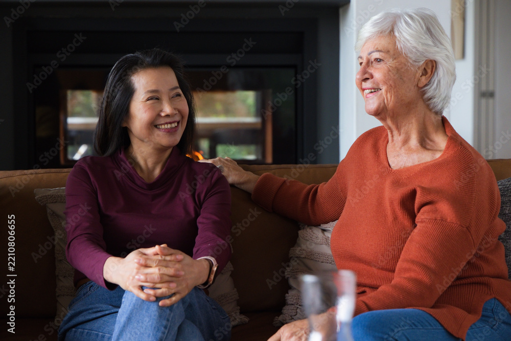 Fototapeta premium Asian mature woman and Senior woman sitting on sofa in living room with fireplace, pillows, smiling