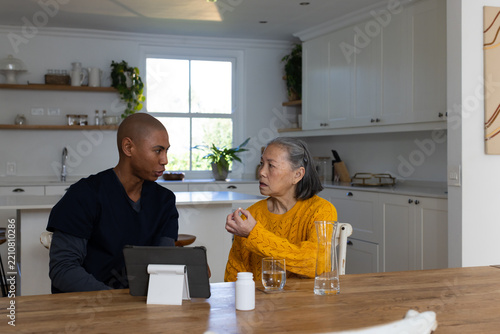 Senior Asian woman yellow-sweater holding orange med bottle, aide using tablet at home