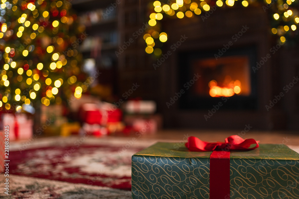 Obraz premium Green gift box in classical Christmas decorated interior living room library with fireplace. Christmas gift near fir tree on Christmas eve. Modern classic style interior design apartment. Christmas