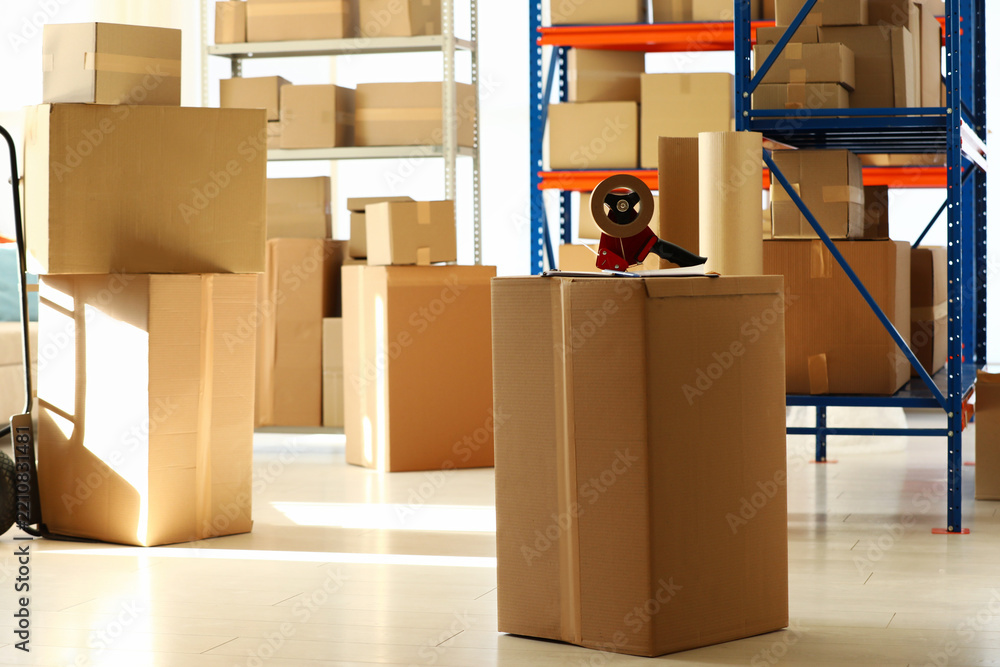 Fototapeta premium Shelves with many cardboard boxes and adhesive tape in warehouse