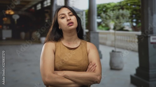 Woman with arms crossed at a building colonnade showing a skeptical pout and folded posture; annoyance defiance.