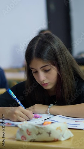 Focused student writing in a notebook during a classroom lesson with peers in the background