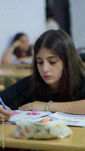 Focused student writing in a notebook during a classroom lesson with peers in the background