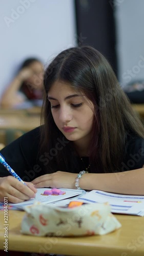 Focused student writing in a notebook during a classroom lesson with peers in the background