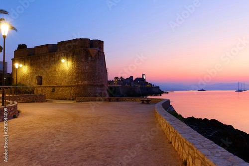 Illuminated stone bastion and seafront promenade at dusk with Antibes Old Town , French Riviera, France