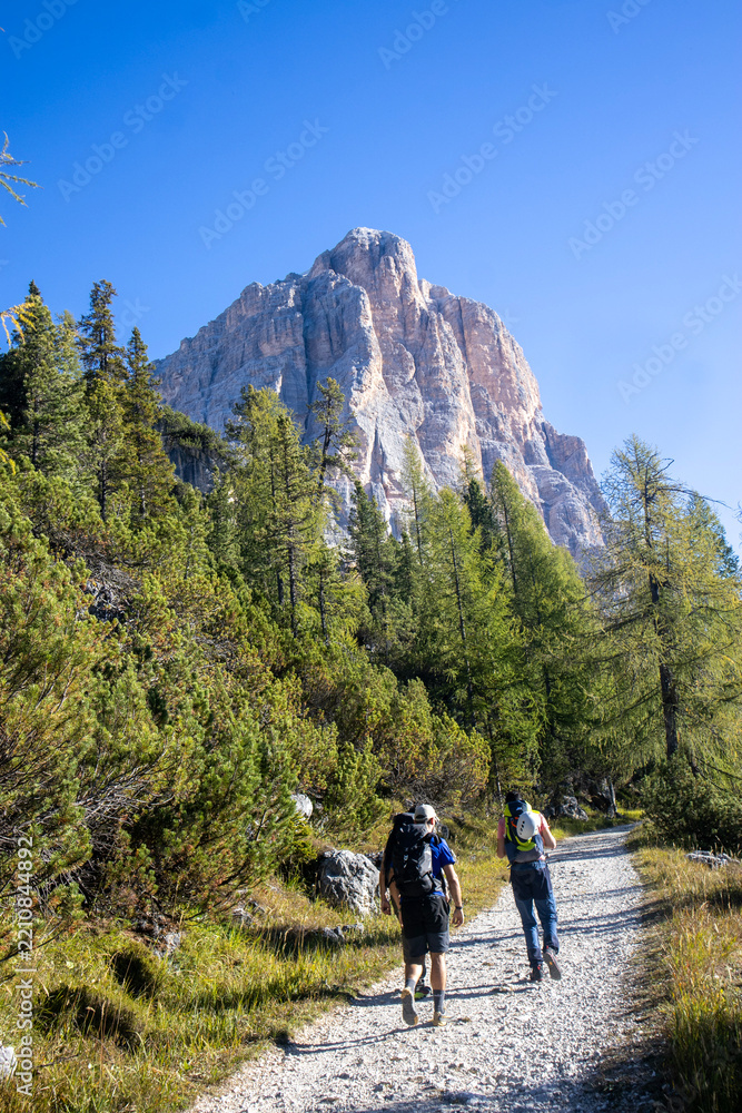 Obraz premium Two hikers on a gravel trail heading towards a massive mountain peak