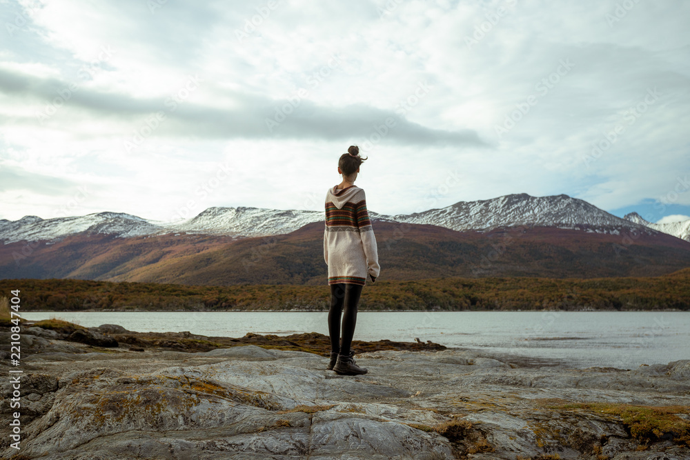 Obraz premium Woman standing on a rocky shore looking towards mountains and water in a natural landscape during daytime