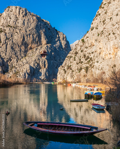 Traditional wooden boat floating on calm Cetina river in rocky canyon, Omis, Croatia