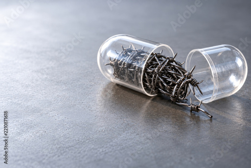 Open transparent capsule contains tangled barbed wire. Space for text.
