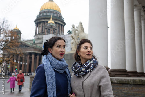 Two women walking in Saint Petersburg city street with Saint Isaac Cathedral in background overcast weather urban lifestyle scene, Saint-Petersburg, Russia