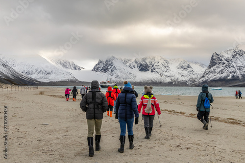 Expedition tourists walking across a remote Arctic beach toward a passenger ship with glacier and snow-covered mountains ahead, Spitsbergen, Svalbard, Norway